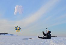 Jenni-Juulia sits on the snowy tundra, flying a yellow kite marked with the ISA symbol.
