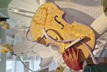 A violin is made of golden brocade fabric. C-cassette has been pushed through the top of a violin