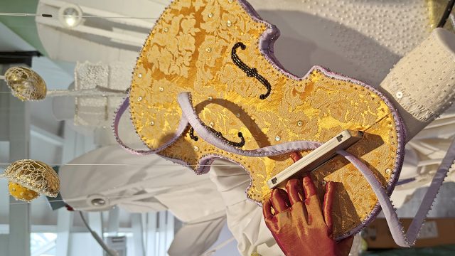 A violin is made of golden brocade fabric. C-cassette has been pushed through the top of a violin