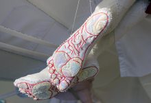 A close-up of two soles of feet from below. They are made of textile material using embroidery and are partially covered with sequins.